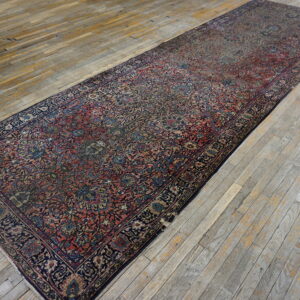 A narrow runner rug featuring dark red and blue traditional patterns lies on weathered gray wood plank flooring.