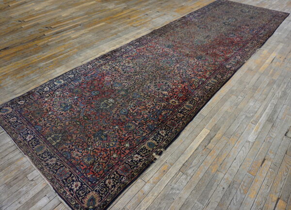 A narrow runner rug featuring dark red and blue traditional patterns lies on weathered gray wood plank flooring.