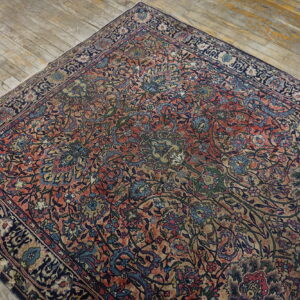 Distressed coral and navy floral rug with an intricate pattern rests on light, rustic hardwood floors.