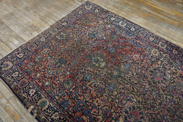 Distressed coral and navy floral rug with an intricate pattern rests on light, rustic hardwood floors.