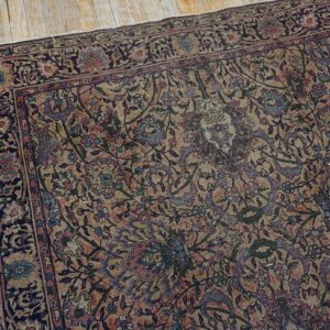 Intricate traditional rug in faded tan, navy, red, and blue floral motifs rests on distressed wood planks.