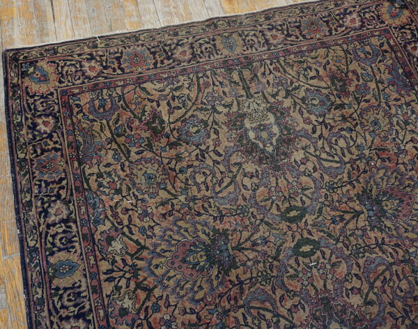Intricate traditional rug in faded tan, navy, red, and blue floral motifs rests on distressed wood planks.