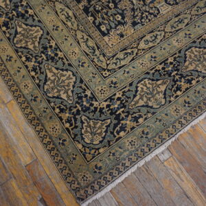 Dark blue and beige rug with intricate floral patterns and green borders rests on distressed wood flooring.