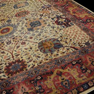 Angled close-up of a low-pile rug with a detailed cream field and deep red and navy blue border.