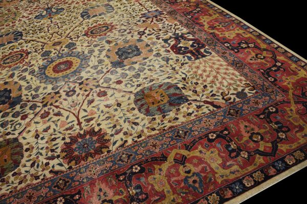 Angled close-up of a low-pile rug with a detailed cream field and deep red and navy blue border.