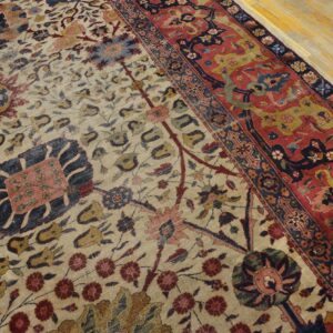 Beige floral rug with red and navy borders, shown up close on light yellow hardwood flooring.
