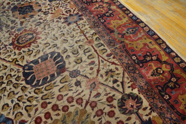 Beige floral rug with red and navy borders, shown up close on light yellow hardwood flooring.