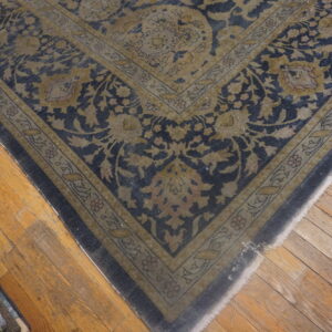 Traditional rug corner featuring navy and dull gold floral patterns on wide plank wooden flooring.