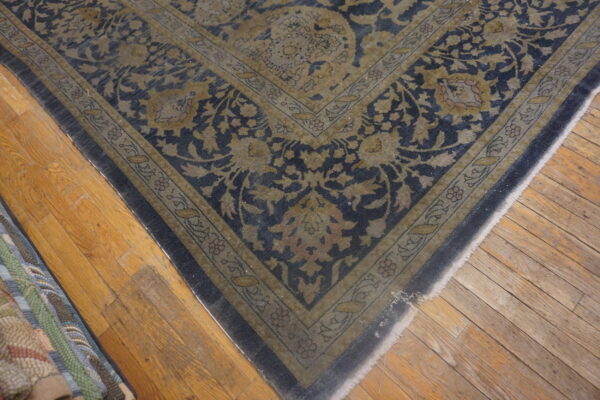 Traditional rug corner featuring navy and dull gold floral patterns on wide plank wooden flooring.