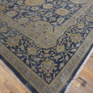 Dark blue and beige floral rug on a worn plank wooden floor with visible fringe.
