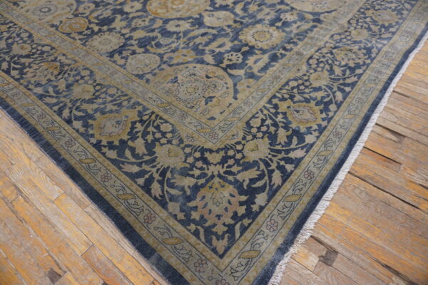 Dark blue and beige floral rug on a worn plank wooden floor with visible fringe.