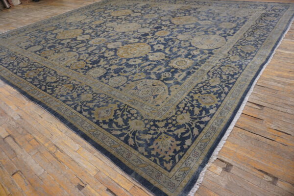 Low-pile rug in blue and tan floral medallion pattern covering rustic wood planks.
