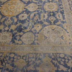 Ornate gold and tan floral patterns overlay a striated navy blue background, highlighting the rug's border design.