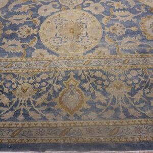 Close-up of a dusty blue rug with tan and gold traditional floral and medallion patterns.