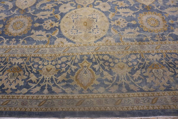 Close-up of a dusty blue rug with tan and gold traditional floral and medallion patterns.