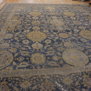 Blue area rug with large muted gold floral medallions and complex borders rests on light wood flooring.