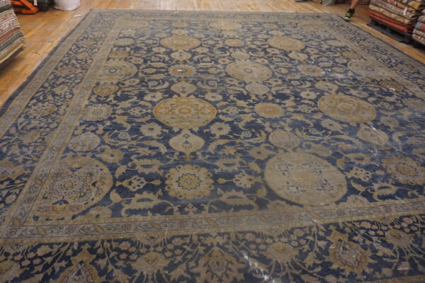 Blue area rug with large muted gold floral medallions and complex borders rests on light wood flooring.