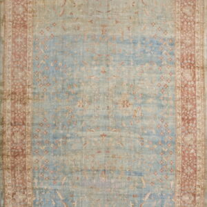 A distressed floral rug features a faded light blue field with tan motifs and a wide rose-colored ornamental border.