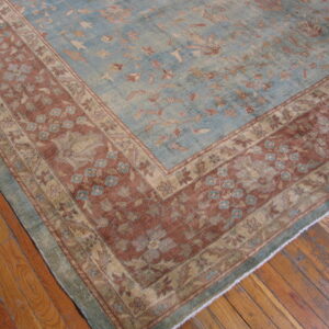Faded blue and rust rug with a traditional floral pattern sits on distressed hardwood plank flooring.