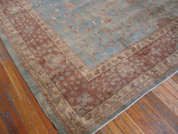 Faded blue and rust rug with a traditional floral pattern sits on distressed hardwood plank flooring.