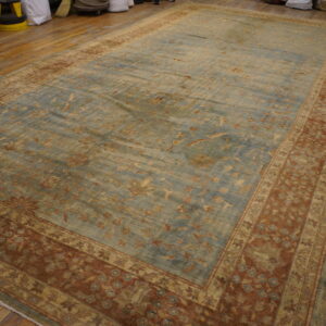A low-pile traditional rug with a faded blue floral field and wide rust borders rests on wood planks.