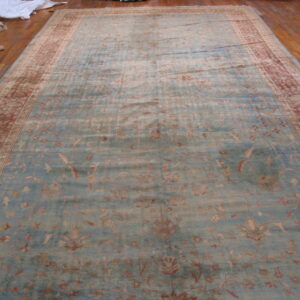 Low-pile blue rug with muted red floral motifs and a wide patterned border on wood floor.