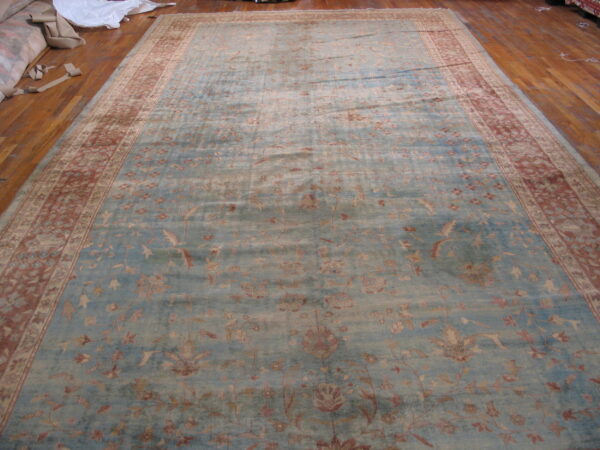 Low-pile blue rug with muted red floral motifs and a wide patterned border on wood floor.