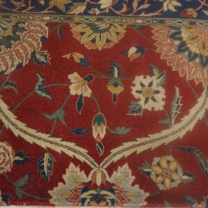 Red rug with a large beige floral medallion and vine pattern on distressed wood flooring.