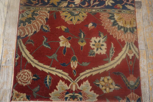 Red rug with a large beige floral medallion and vine pattern on distressed wood flooring.