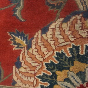 The rug features an ornate pattern of orange, blue, and beige palmettes against a deep red background.
