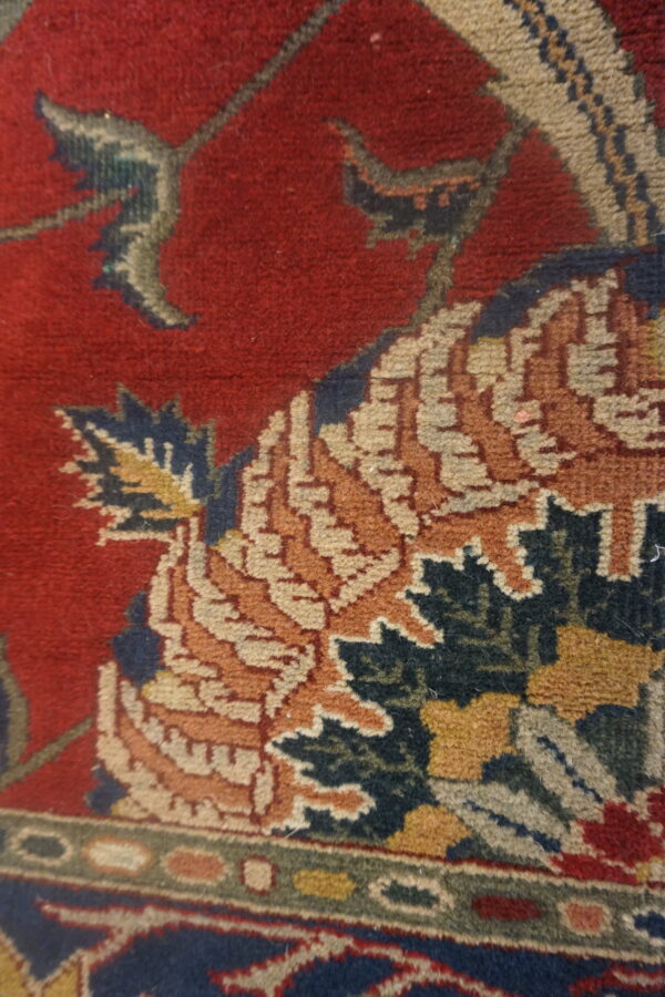 The rug features an ornate pattern of orange, blue, and beige palmettes against a deep red background.