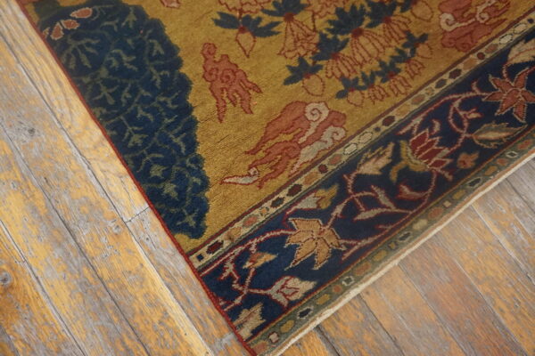 Gold, blue, and rust patterned rug detail resting on heavily distressed light wood flooring.