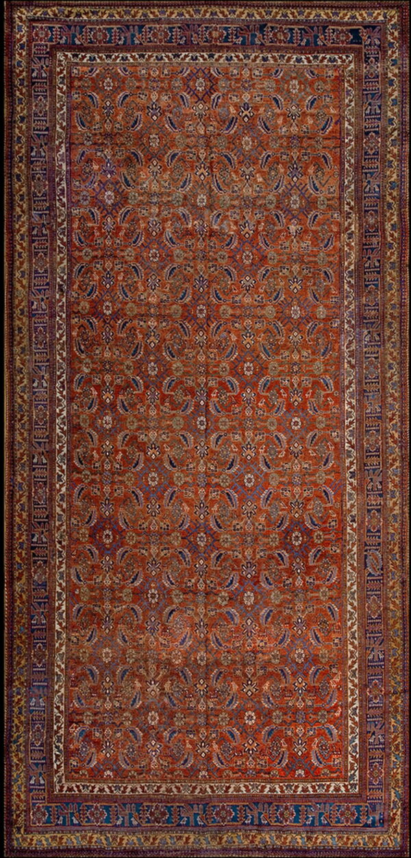 Rust-colored rug with a dense blue and ivory paisley motif and complex multi-layered borders.
