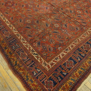 Traditional red rug with navy and gold geometric borders lying diagonally on distressed wood planks.