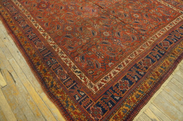 Traditional red rug with navy and gold geometric borders lying diagonally on distressed wood planks.