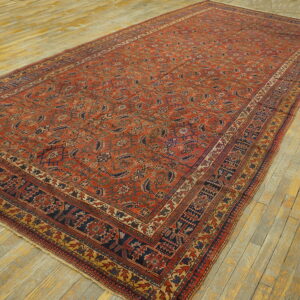 A large rust-red rug featuring repeating navy and beige motifs lies on yellow plank flooring.