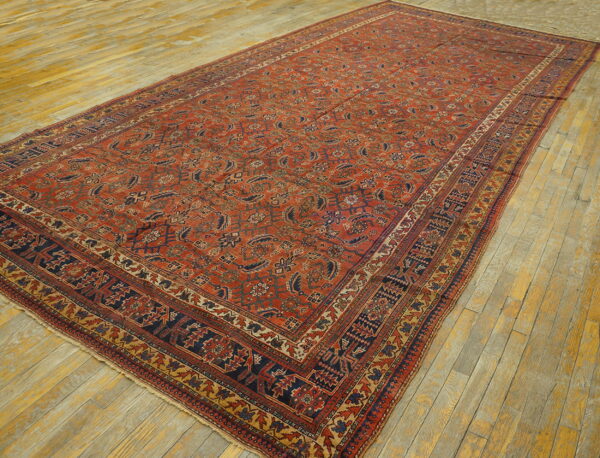 A large rust-red rug featuring repeating navy and beige motifs lies on yellow plank flooring.