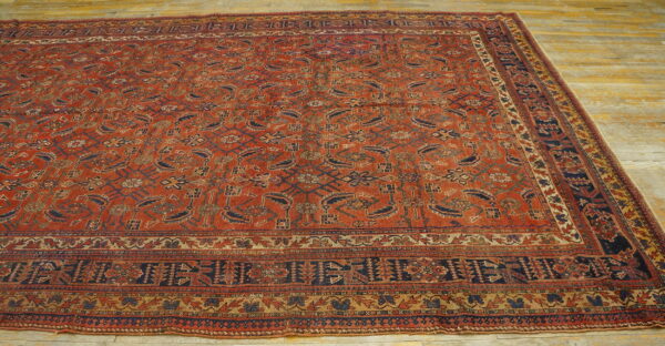 Low-pile rust red area rug featuring dense geometric and floral patterns sits on a wooden floor.