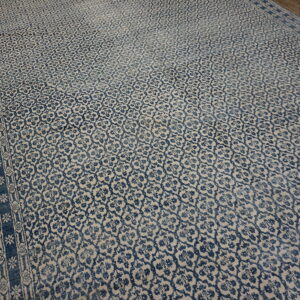 A large blue and beige rug featuring an all-over trellis pattern and geometric borders on wood flooring.