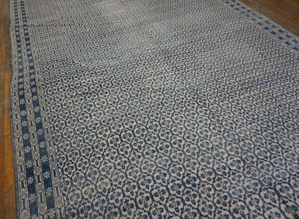 A large blue and beige rug featuring an all-over trellis pattern and geometric borders on wood flooring.