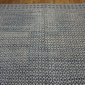 Distressed low-pile blue and beige patterned rug featuring an ornate border, set on wood flooring.