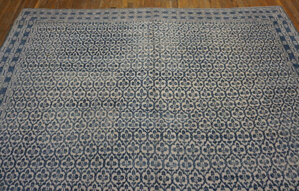Distressed low-pile blue and beige patterned rug featuring an ornate border, set on wood flooring.