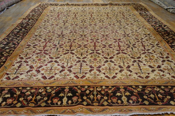 Cream and burgundy botanical rug with dark borders lies flat on a light wood floor.