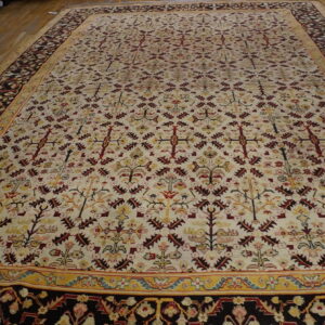 Large rug with cream field, red and yellow traditional repeating patterns, and a dark border on wood floor.