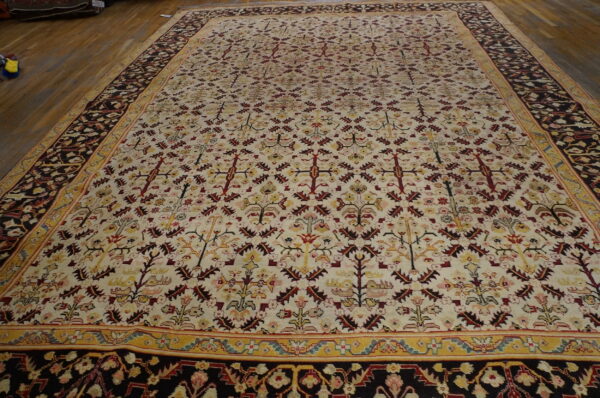 Large rug with cream field, red and yellow traditional repeating patterns, and a dark border on wood floor.