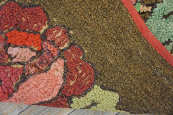 Detail of a high pile rug with red, pink, and green floral motifs on an earthy brown field.