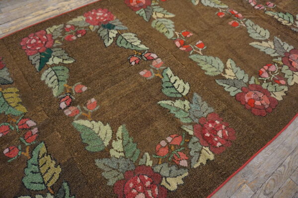 Textured brown rug featuring repeated red rose and green leaf garlands rests on wood plank flooring.