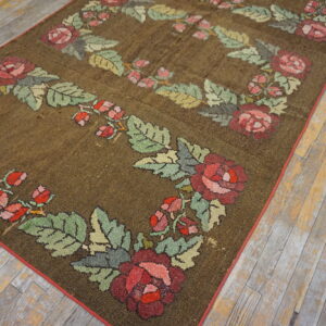 Dark brown textured rug featuring borders of red roses and green leaves on weathered wood flooring.