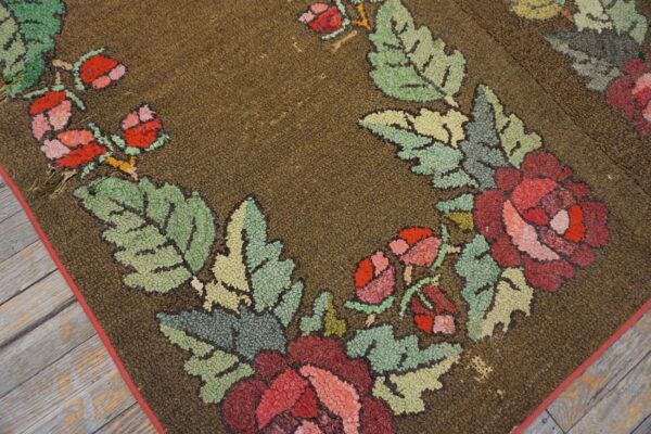 Textured brown rug with a prominent border of red flowers and loopy green leaves on rustic plank flooring.