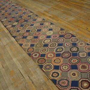 Colorful hooked runner rug featuring concentric octagons and blue squares rests on worn wood flooring.